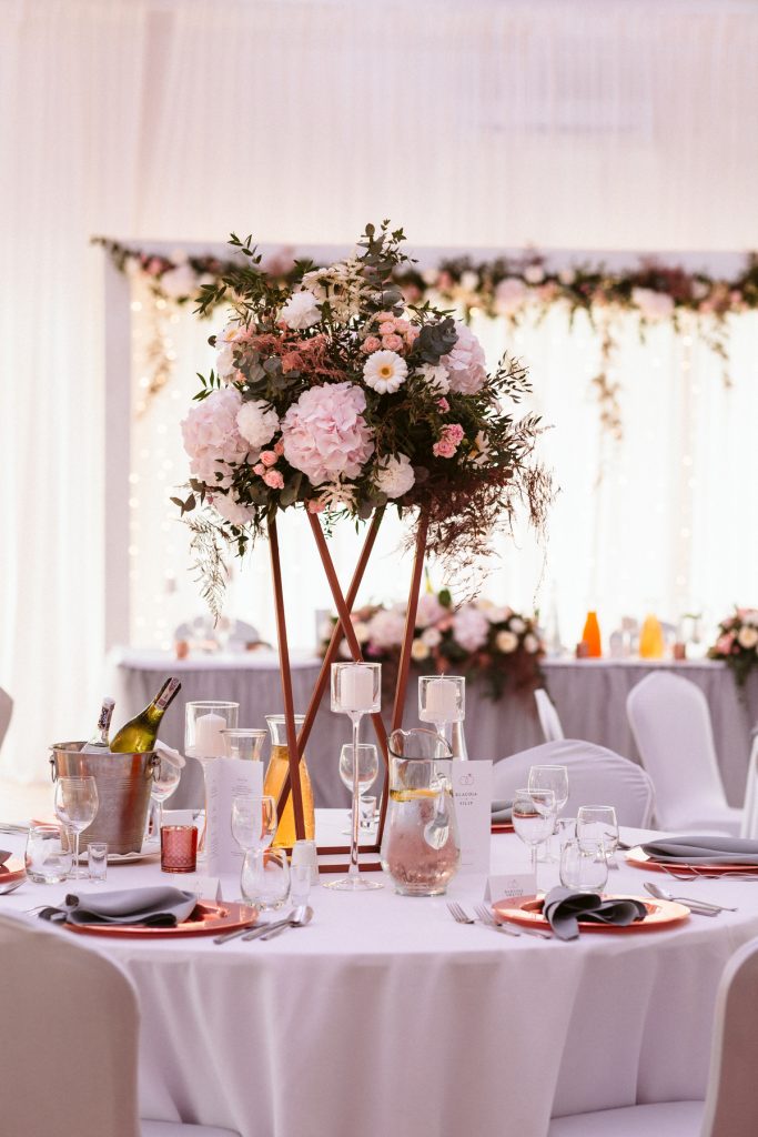 wysoka kompozycja z kwiatów w formie półkuli na krzyżowym miedzianym stojaku jako dekoracja stołu gości