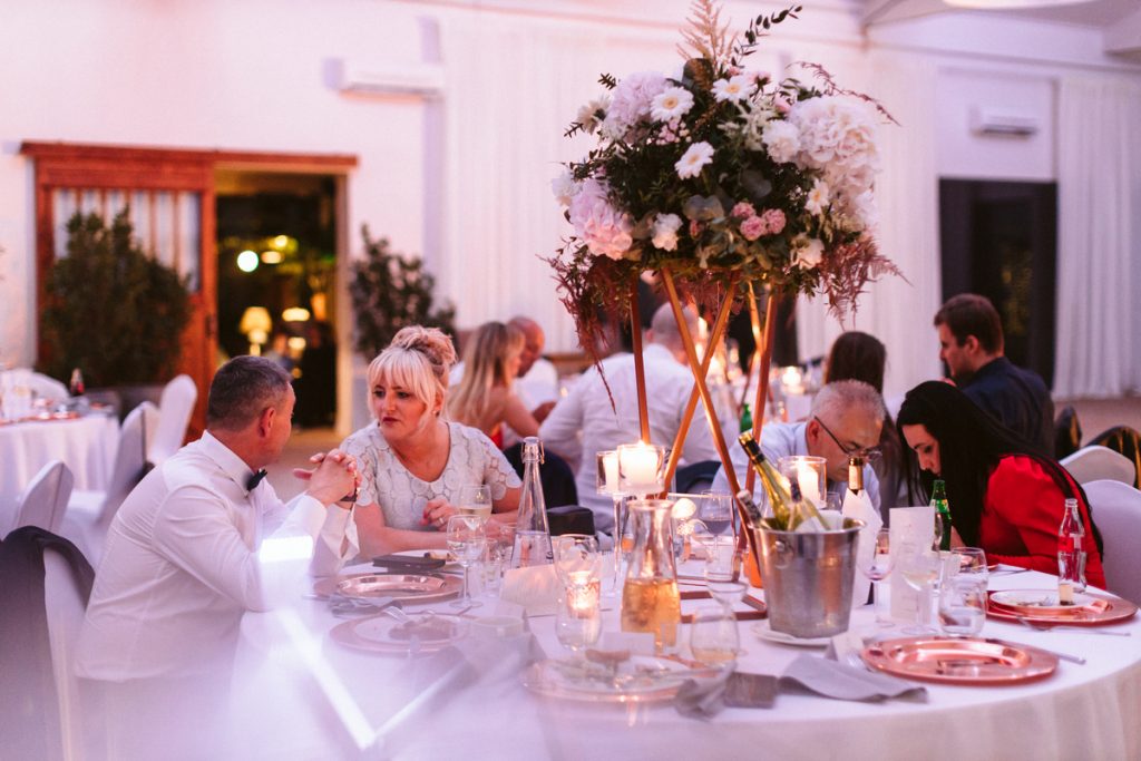 kompozycje kwiatowe na miedzianych stojakach jako dekoracja stołów gości na przyjęcie weselne