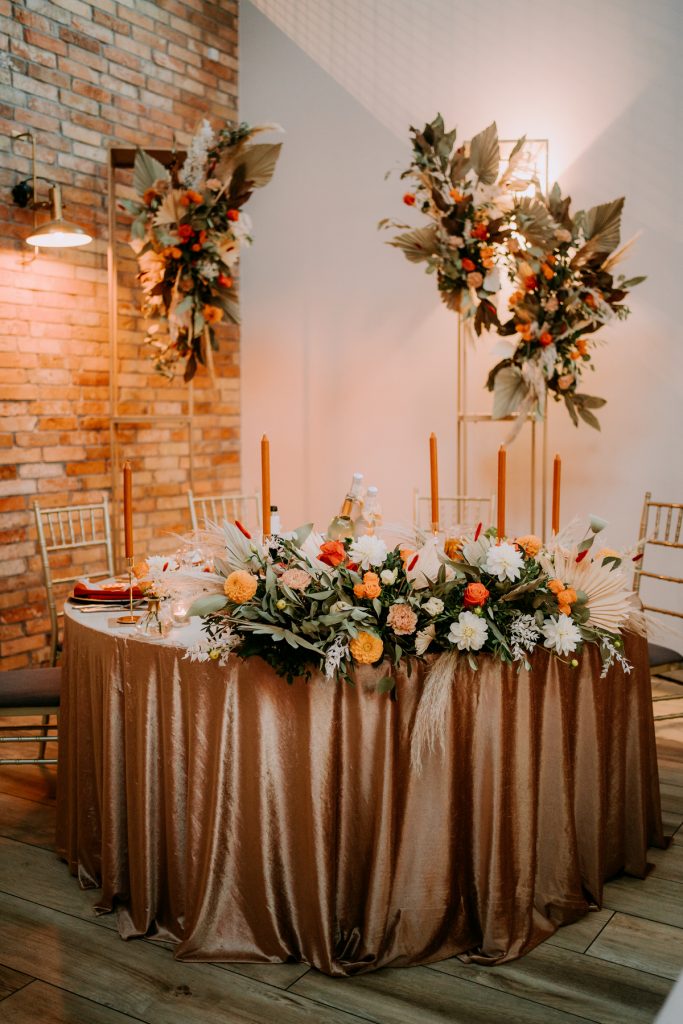 aranżacja stołu pary młodej złotymi geometrycznymi konstrukcjami i welurowym obrusem i rdzawymi długimi świecami