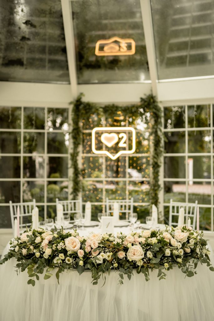 duża kompozycja z zieleni i róż ogrodowych jako główna dekoracja stołu prezydialnego z tiulem