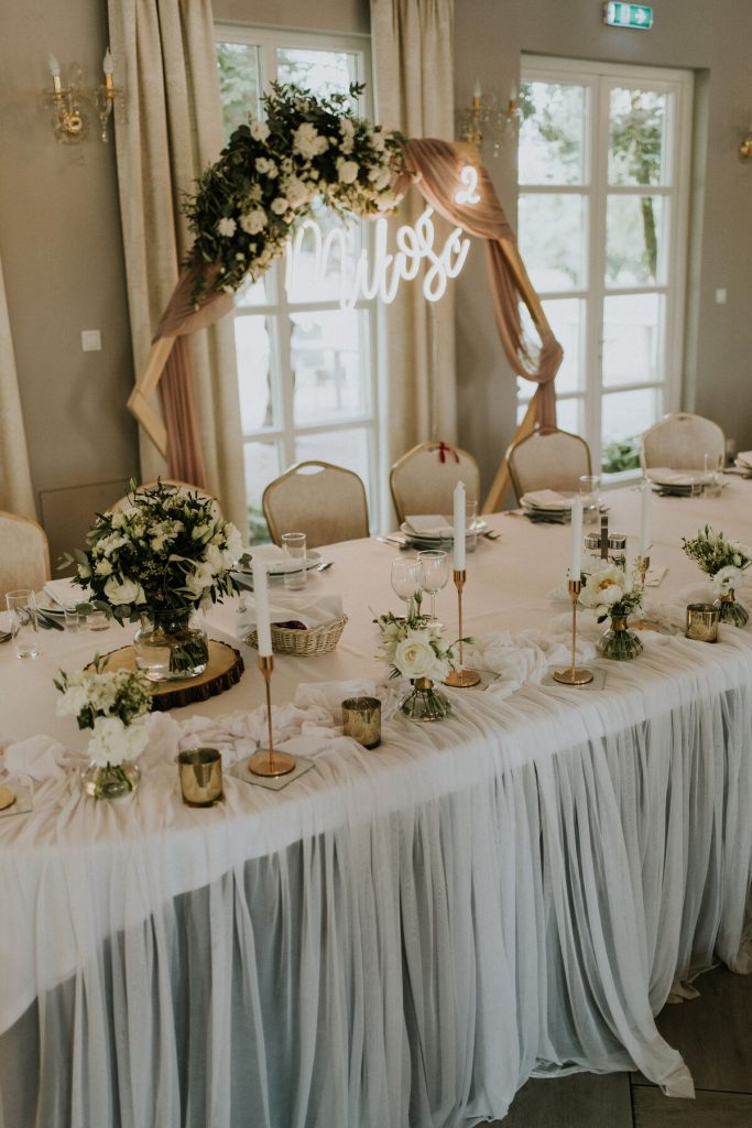 asymetryczna dekoracja stołu prezydialnego zwiewnym materiałem złotymi świecznikami i subtelnymi bukiecikami kwiatów