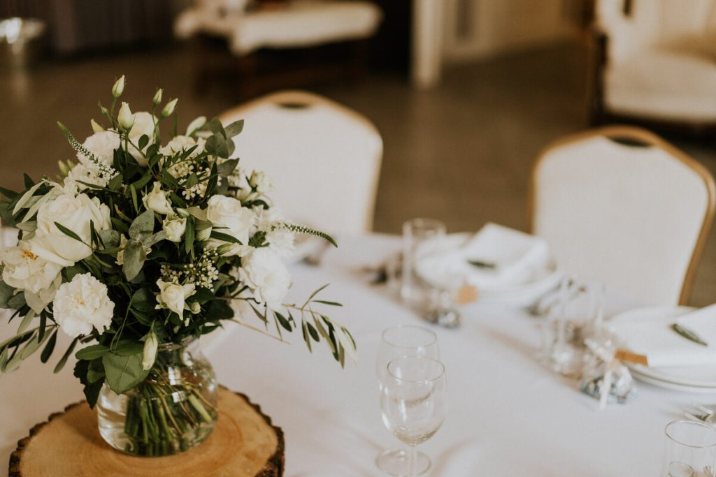 piękny bukiet białych kwiatów z zielenią jako aranżacja okrągłego stołu gości