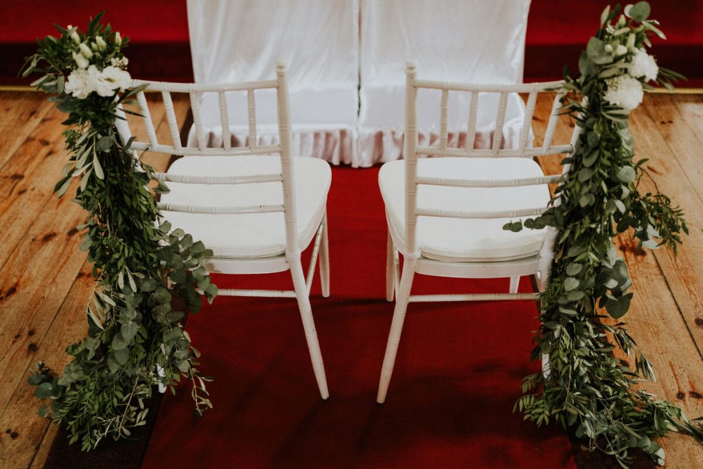 dekoracja krzeseł pary młodej do ślubu zielonymi girlandami i białymi kwiatami
