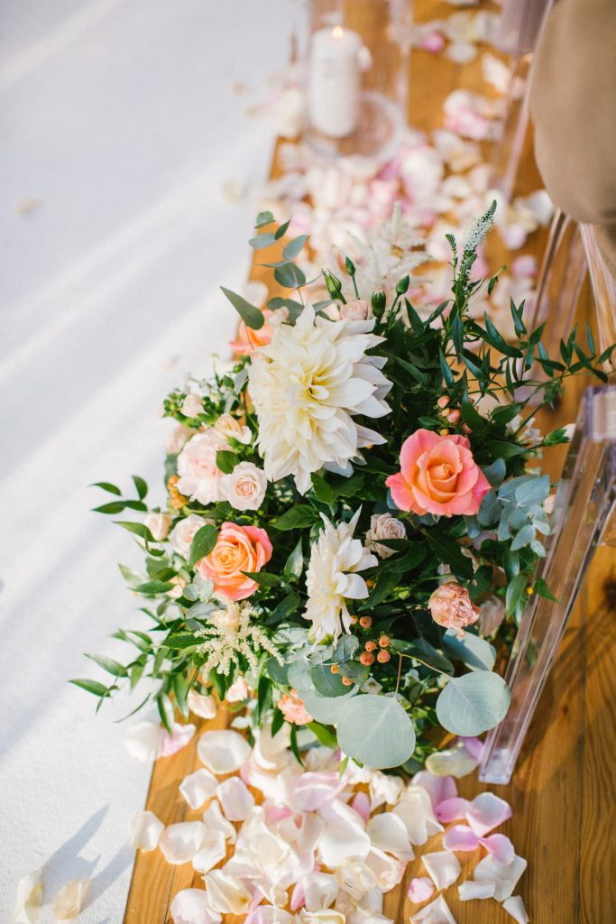 kompozycje z zieleni i kwiatów w kolorze brzoskwiniowo koralowym oraz płatki róż w alejce na ślubie plenerowym
