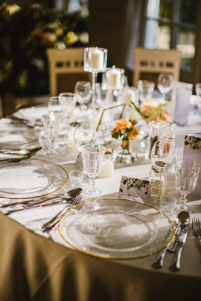 szklane podtalerze ze złotym rantem i brzoskwiniowe dodatki na stole okrągłym gości